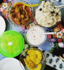 Photo showing a meal of ghee rice, chicken curry, raita, and pineapple. 